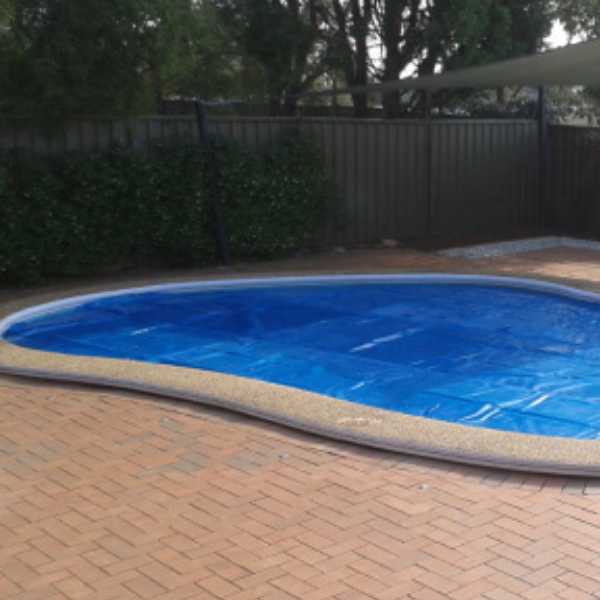 Exemplo do uso da capa térmica para piscina na cor azul, elaborada sob medida para piscina oval